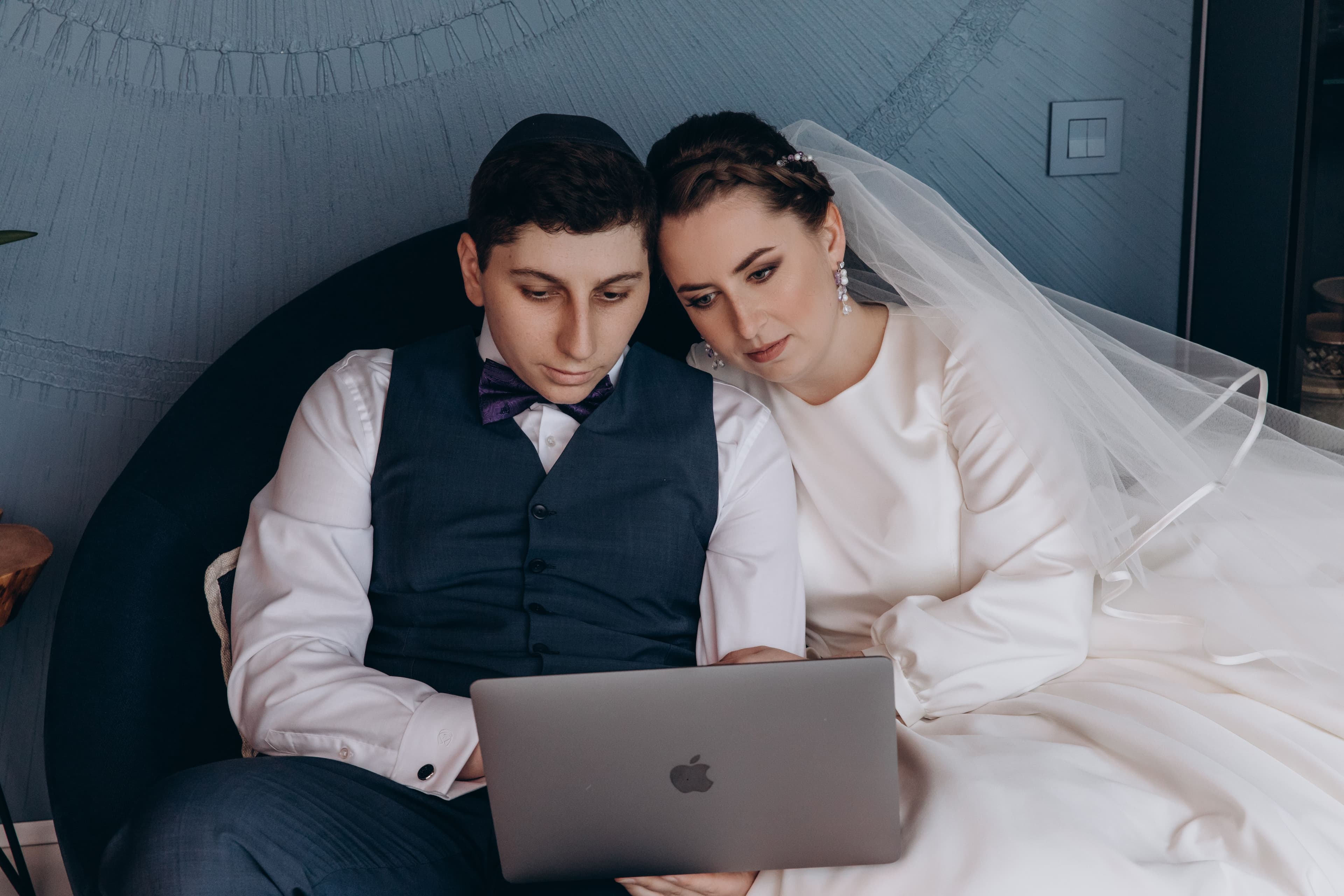 Bride and groom smiling while setting up their shared photo album on a laptop